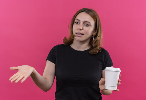 空困惑的年轻随意的女人拿着塑料咖啡杯 在孤立的粉色空间里空手而出年轻困惑手