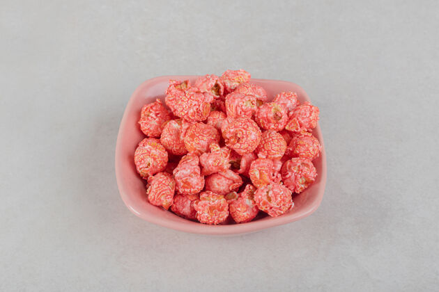 碗放在大理石桌上粉红色盘子上的一小堆有香味的爆米花垃圾食品外套不健康