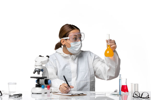 外套正面图：女医生 穿着特制的工作服 戴着口罩 拿着装有黄色溶液的烧瓶 在白色背景上写着大流行冠状病毒实验室外套保持女医生