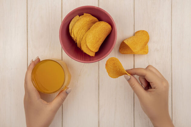 食物女性手拿美味脆薯片和一杯橙汁放在米色木桌上的俯视图薯条橘子小吃