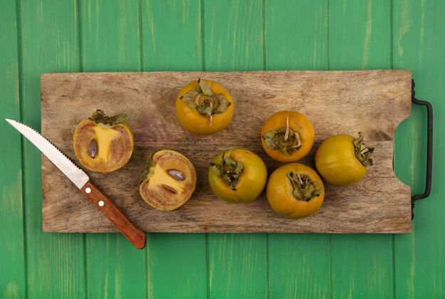 顶部新鲜柿子水果的顶视图在一个木制的厨房板上用刀放在一张绿色的木桌上景观水果新鲜