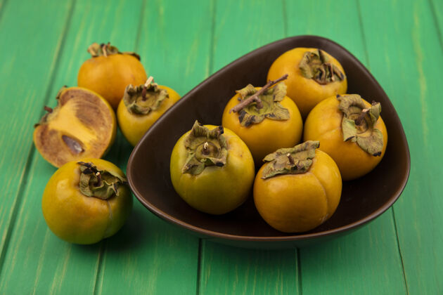 绿色健康和新鲜的柿子水果在一个绿色的木桌碗顶视图橙色木材新鲜