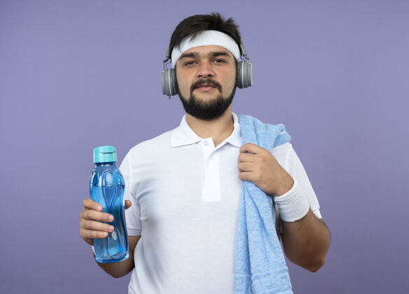 瓶子喜欢运动的年轻人戴着头带和腕带 头戴耳机 肩上扛着毛巾的水瓶头带手握运动型