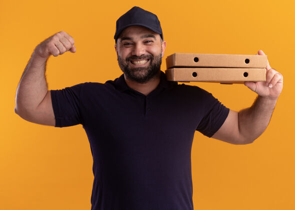 抱着微笑的中年送货员身着制服 戴着帽子 肩上扛着披萨盒 在黄色的墙上显示出强烈的姿态盒子肩膀送货