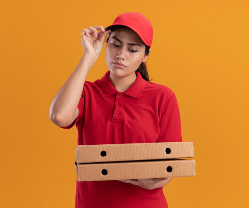 女孩想着那个穿着制服 戴着帽子的年轻送货女孩 看着隔离在橙色墙上的披萨盒 手里拿着帽子披萨穿思考