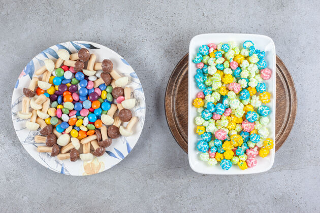 零食一盘糖果和巧克力蘑菇 旁边是一盘爆米花糖果 放在大理石表面的木制托盘上托盘糖果美味