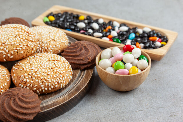 饼干把饼干堆在木板上 旁边是一个碗里的成堆糖果和大理石表面的木托盘糖糕点碗