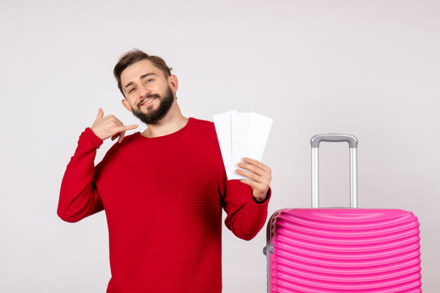 颜色正面图：年轻男性 带着粉色包 手持白墙彩色旅游机票 度假旅游旅游年轻的男性机票