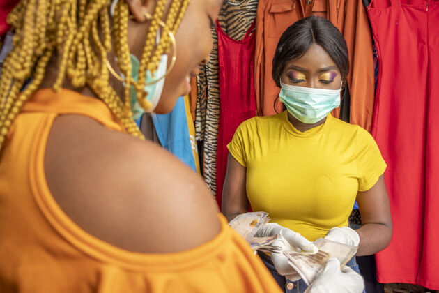 购物特写镜头：一位非洲女性戴着乳胶手套和口罩 在一家商店用现金付款销售联系人女人
