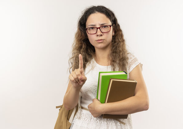 眼镜年轻漂亮的女学生戴着眼镜 背着书包 举着手指 在白色的背景上孤立着 留着复印空间漂亮手指年轻