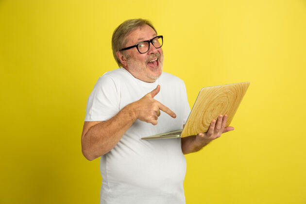 时尚使用笔记本电脑 指向黄色工作室背景上隔离的白种人肖像穿着白衬衫的漂亮男模摆姿势人类情感的概念 面部表情 销售 广告复制空间职业养老金面部