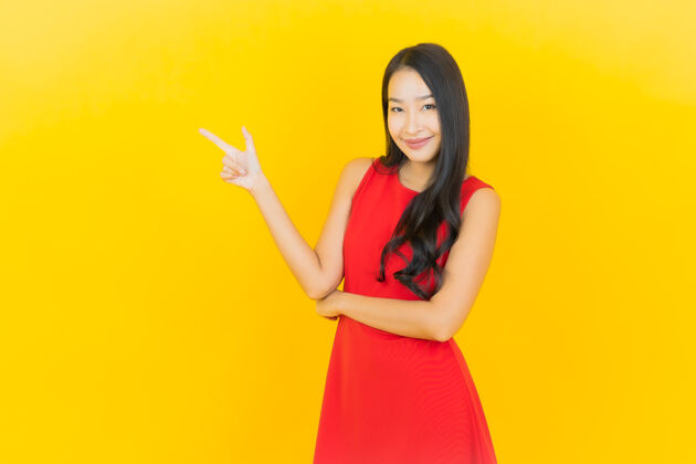 黑发肖像美丽的亚洲年轻女子穿着红色连衣裙微笑着行动在黄色的墙上时尚微笑肖像