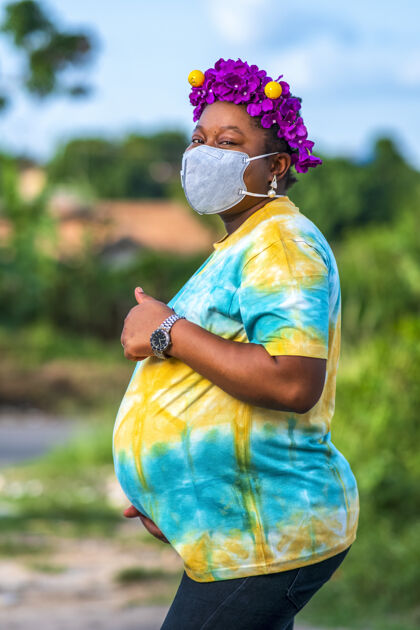 新怀孕的非洲裔美国女性戴着防护面罩 打着竖起大拇指的手势垂直年轻医疗保健