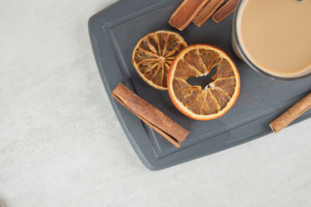 热的美味的咖啡 肉桂条和橘子片放在深色盘子里水果香味肉桂