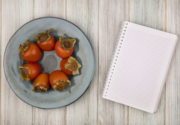 盘子在灰色木质背景上的盘子上放着柔软的新鲜柿子 上面有复制空间新鲜副本笔记本