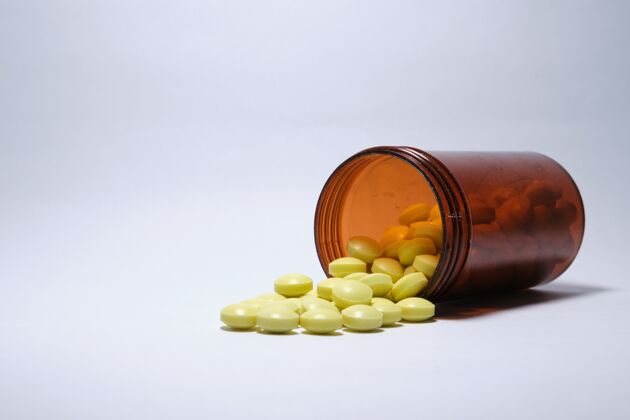 瓶子黄色药片的特写镜头从白色背景上的棕色瓶子里掉了出来药品健康塑料