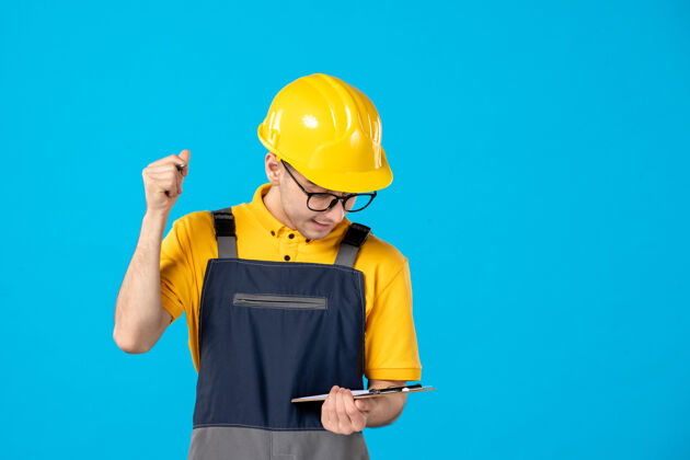 男身穿制服和头盔的男建筑工人在蓝色墙上做笔记的正面图工人水管工人