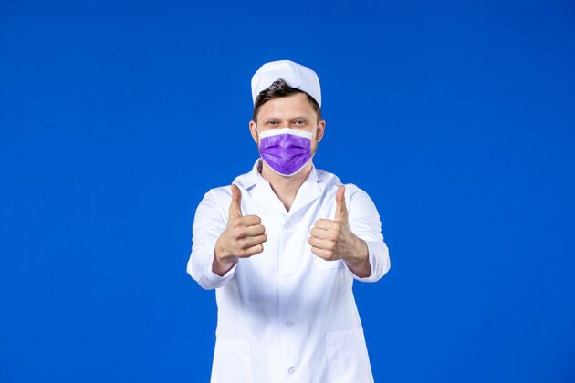 视图身着医疗服 戴着紫色面具的男医生在蓝色墙上的正视图疫苗人病毒