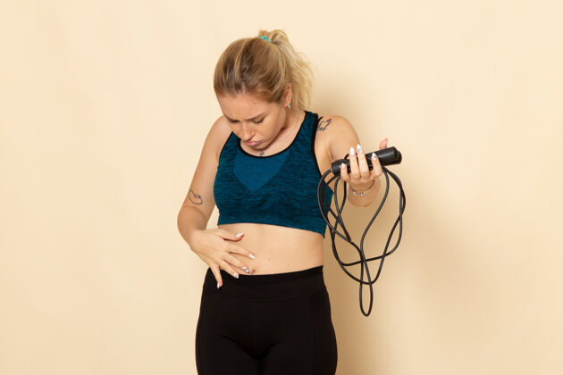 烘干机正面图身着运动装的年轻女性手持跳绳在白墙上健康锻炼身体运动美容操吹风机肖像成人