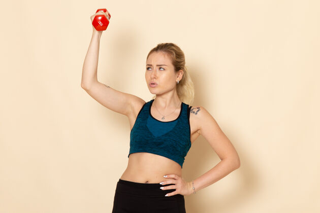 健身正面图身穿运动装的年轻女性手持红色哑铃站在白墙上运动身体健康美容锻炼的女人身体年轻女性体重