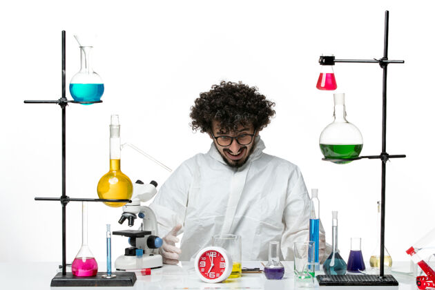 套装正面图穿着特殊套装的年轻男性科学家坐在浅白的墙上 拿着解决方案科学罐子化学