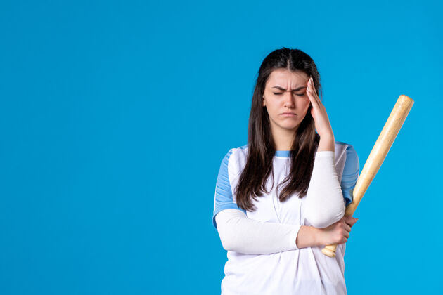 年轻女性正面图蓝色墙上拿着棒球棒的年轻女子体育蓝色棒球