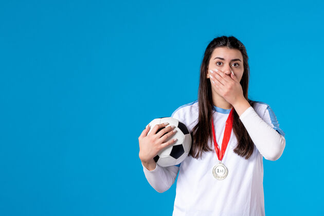 体育前视图：年轻女子在蓝色墙上拿着足球足球肖像正面