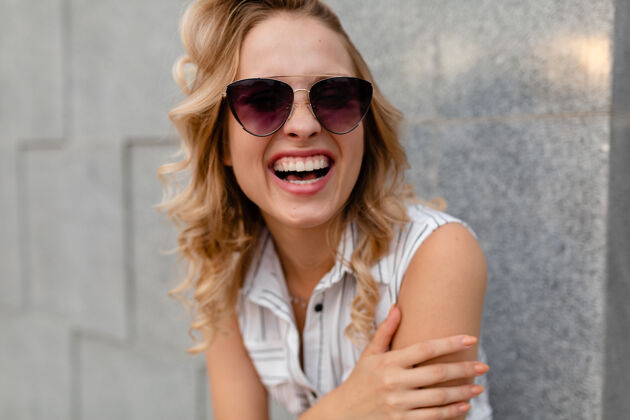 白色年轻迷人的时尚女性微笑的肖像穿着夏日时尚的连衣裙戴着墨镜走在城市街道上坦诚的微笑正面牙齿微笑