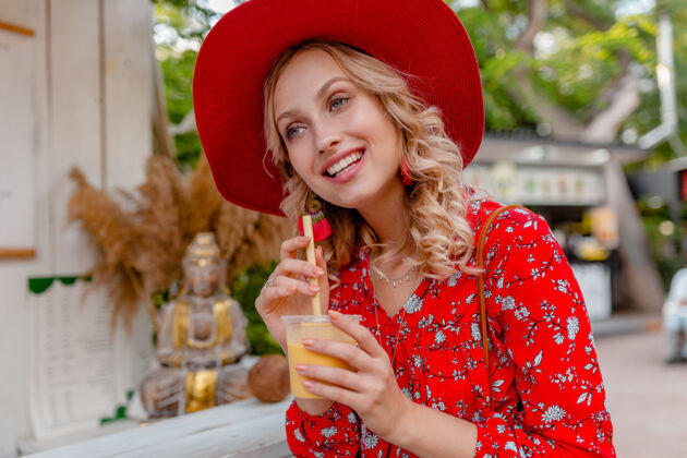 时尚迷人时尚的金发微笑女士 头戴草帽 身穿短衫 夏季时尚套装 饮用天然水果鸡尾酒冰沙女性女孩明亮