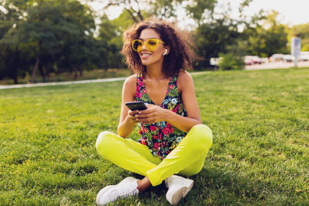 女孩年轻时尚微笑的黑人女子使用智能手机 通过无线耳机听音乐 在公园里玩得很开心女人黑色兴奋