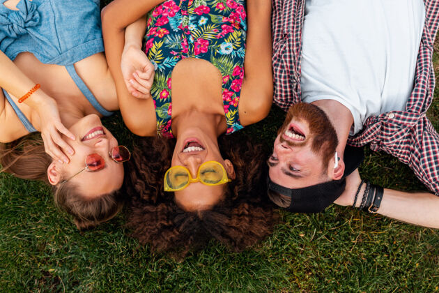 情绪俯瞰五颜六色时尚快乐的年轻朋友们躺在公园的草地上 男女同乐团体女孩朋友