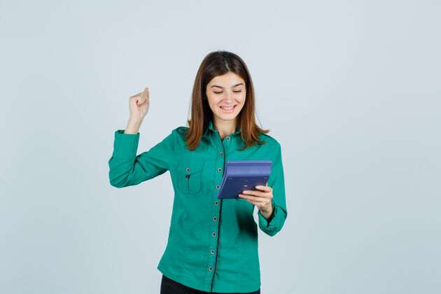欢呼拿着计算器的年轻女士的肖像 展示着身着绿色衬衫的赢家姿态 看着幸福的前景色计算器前面肖像