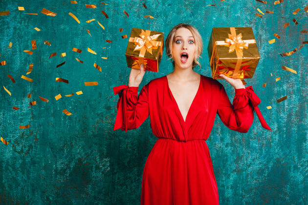 五彩纸屑穿着时尚红色连衣裙的迷人惊艳女子 用礼物庆祝圣诞节和新年乐趣年轻礼物
