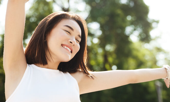 满意亚洲女人举手微笑的特写镜头 漫步在公园里 看起来无忧无虑 幸福快乐微笑自然休闲