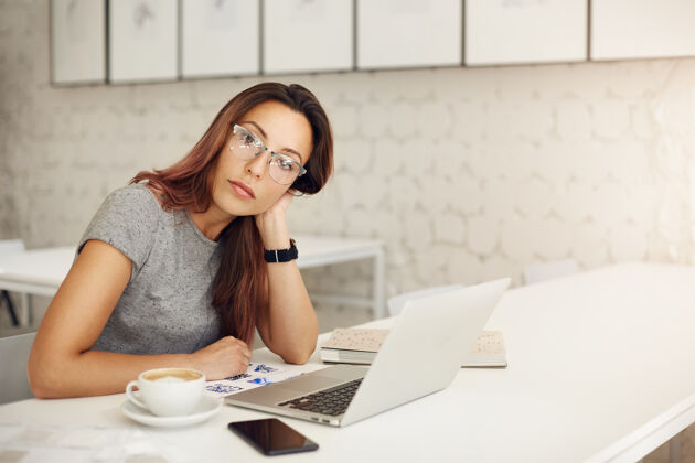 立场女企业家经营一个成功的网上商店使用笔记本电脑戴眼镜在一个宽敞的工作室或咖啡馆自由职业者的概念女孩在线笔记本电脑