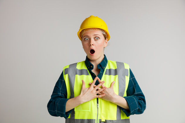 白色吓得年轻的女建筑工人戴着安全帽和安全背心 双手放在胸前看着侧面工人建筑保持