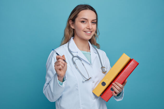 文件夹面带微笑的年轻女医生 穿着医用长袍 脖子上戴着听诊器 手里拿着笔和文件夹持有微笑穿