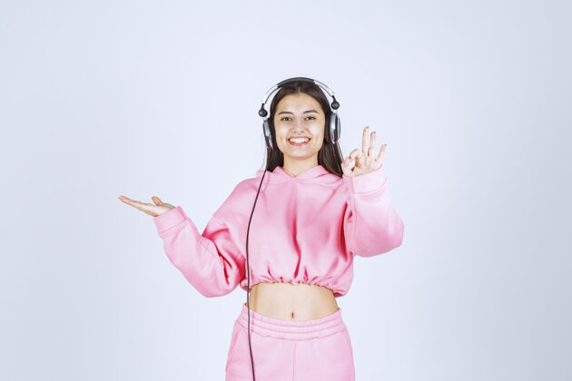 女性穿着粉色睡衣的女孩戴着耳机 展示着享受的标志高质量的照片交易娱乐人体模特