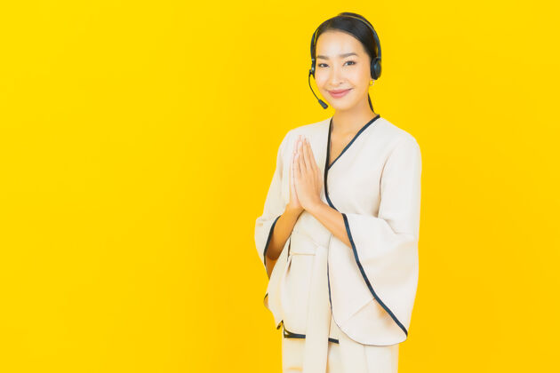 东方人黄色墙上挂着一幅美丽年轻的亚洲商务女士的画像 她戴着耳机为呼叫中心客户服务通信接线员商务女性