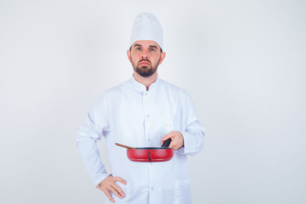 厨师年轻的男厨师手拿煎锅和木勺 身穿白色制服 表情严肃的正面照片职业人健康
