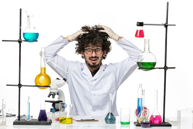 化学前视图穿着医疗服的男性化学家正坐在桌子前面 空白处有溶液医学科学病毒