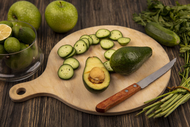 肥肉顶视图黄瓜片放在木制的厨房板上 鳄梨和小刀放在玻璃碗上 绿色的苹果和欧芹被隔离在木制的表面上食物新鲜玻璃
