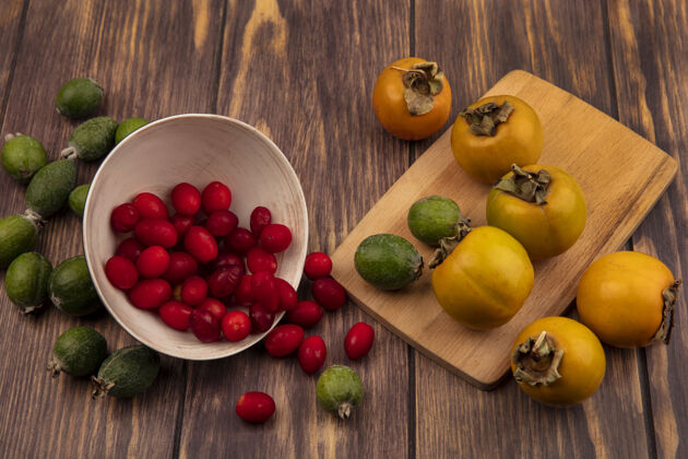 樱桃俯视图：美味的茱萸樱桃和柿子一起从碗里掉出来 放在木制的厨房板上碗配料健康