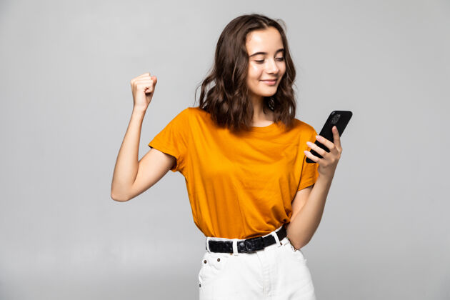 沟通一个满意的年轻女子手持手机 在格雷上空庆祝孤立的肖像短信科技成功