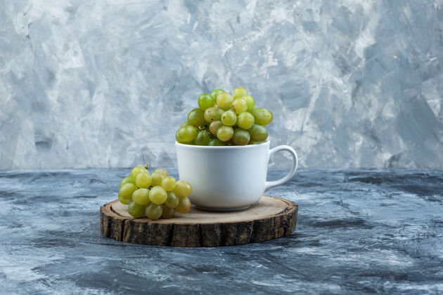 树叶侧视图绿色葡萄在白色的杯子上 在粗糙的石膏和木片背景上水平有机组成树枝