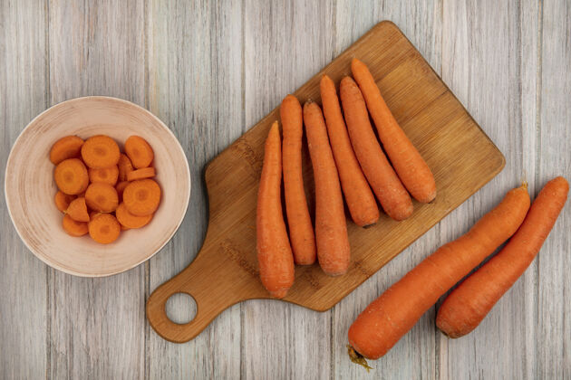 木材顶视图橙色根蔬菜胡萝卜在一个木制的厨房板上切碎的胡萝卜在一个灰色的木制表面碗人板根