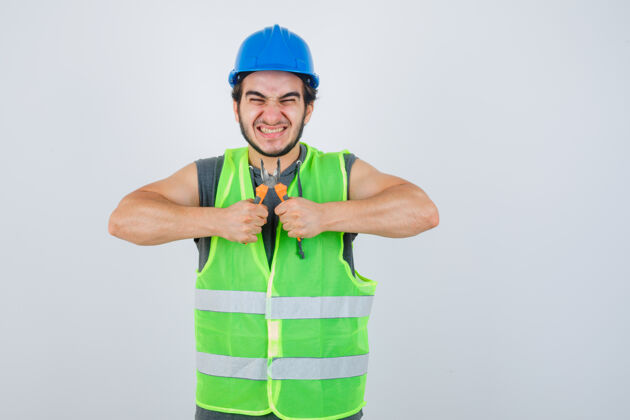 人年轻的建筑工人穿着工装 手里拿着钳子 看上去很高兴 前视图钳子男人模特