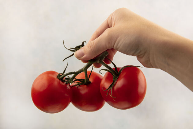 有机白色表面上手持新鲜红色西红柿的女性手的俯视图保持配料美味