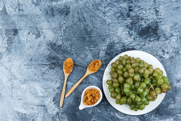 葡萄藤一组葡萄干和绿葡萄放在一个白色的盘子里 背景是灰泥顶视图成熟美味新鲜