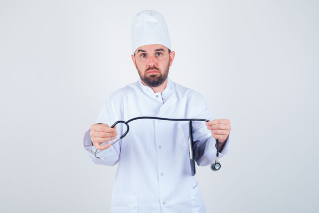 不确定年轻的男医生拿着剪贴板和听诊器 穿着白色制服 面带疑惑 正前方视图护理不知所措剪贴板